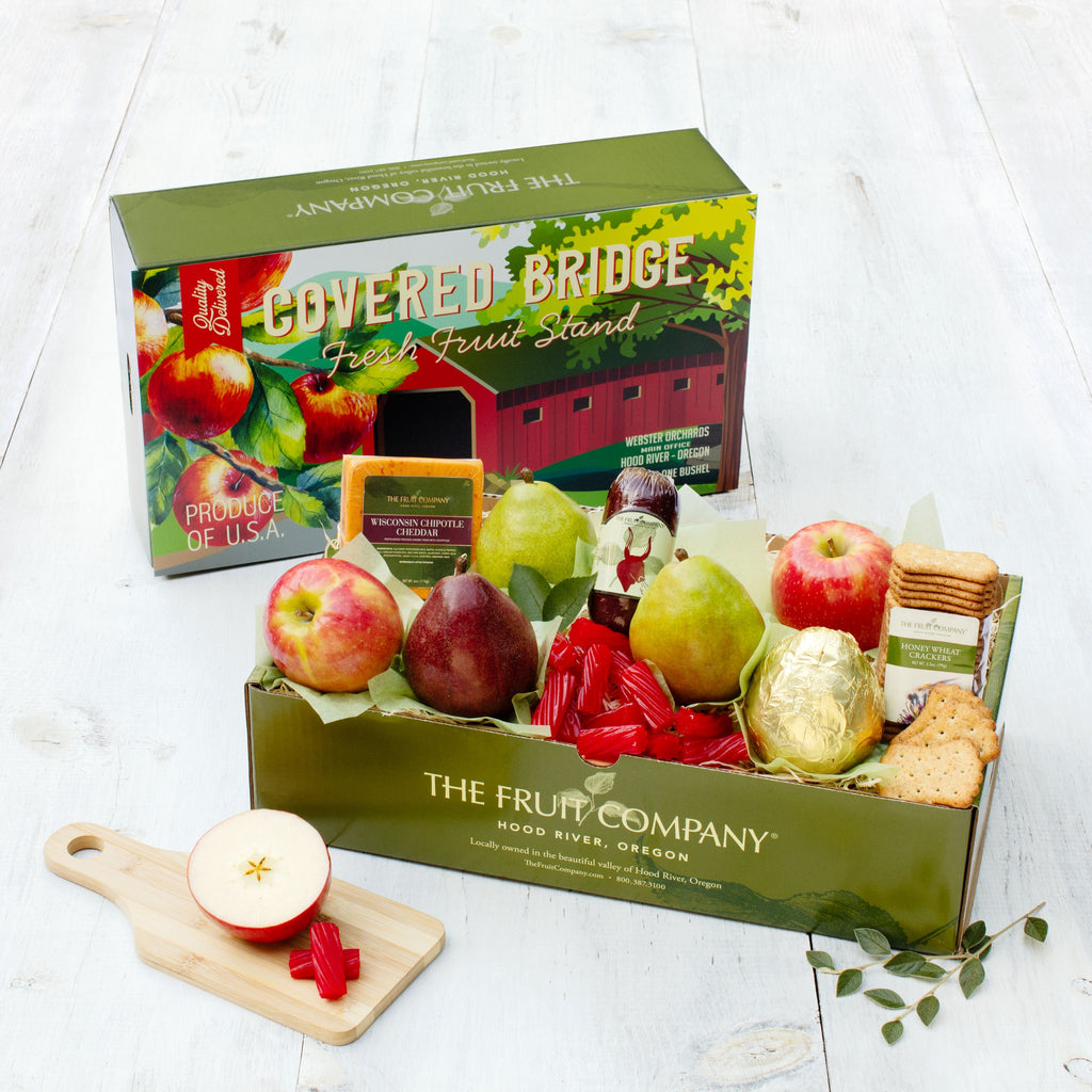 Vintage Covered Bridge-themed box lid filled with fresh fruit, meat, cheese and other treats