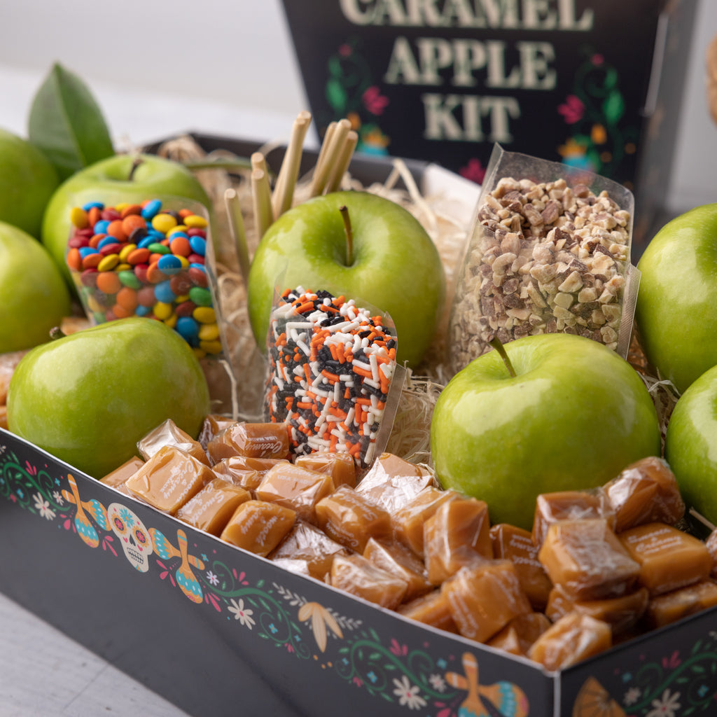 Recipe card for the Caramel Apple Kit A person holding the Caramel Apple Kit  Apple, candies, and caramels in a festive box Coffin shaped caramel apple kit for dia de muertos Caramel apples with M&M's and nuts M&M's and green apples in a festive box Caramels, candies, and green apples in a festive box Bags of candy in the Dia de Muertos box Openned transparent bag of M&M's